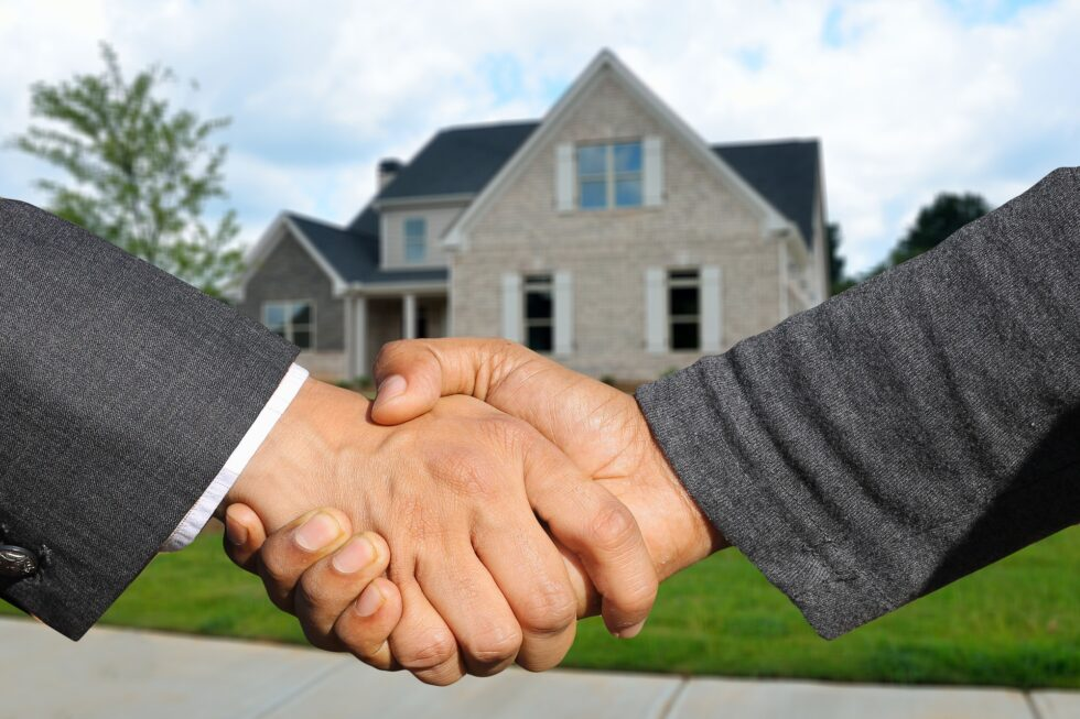 Two people shaking hands in front of a modern house, symbolizing a real estate agreement or partnership. the focus is on the handshake with the home in the background.