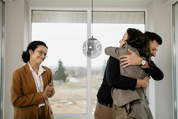 Couple Hugging Each Other beside a Real Estate Agent